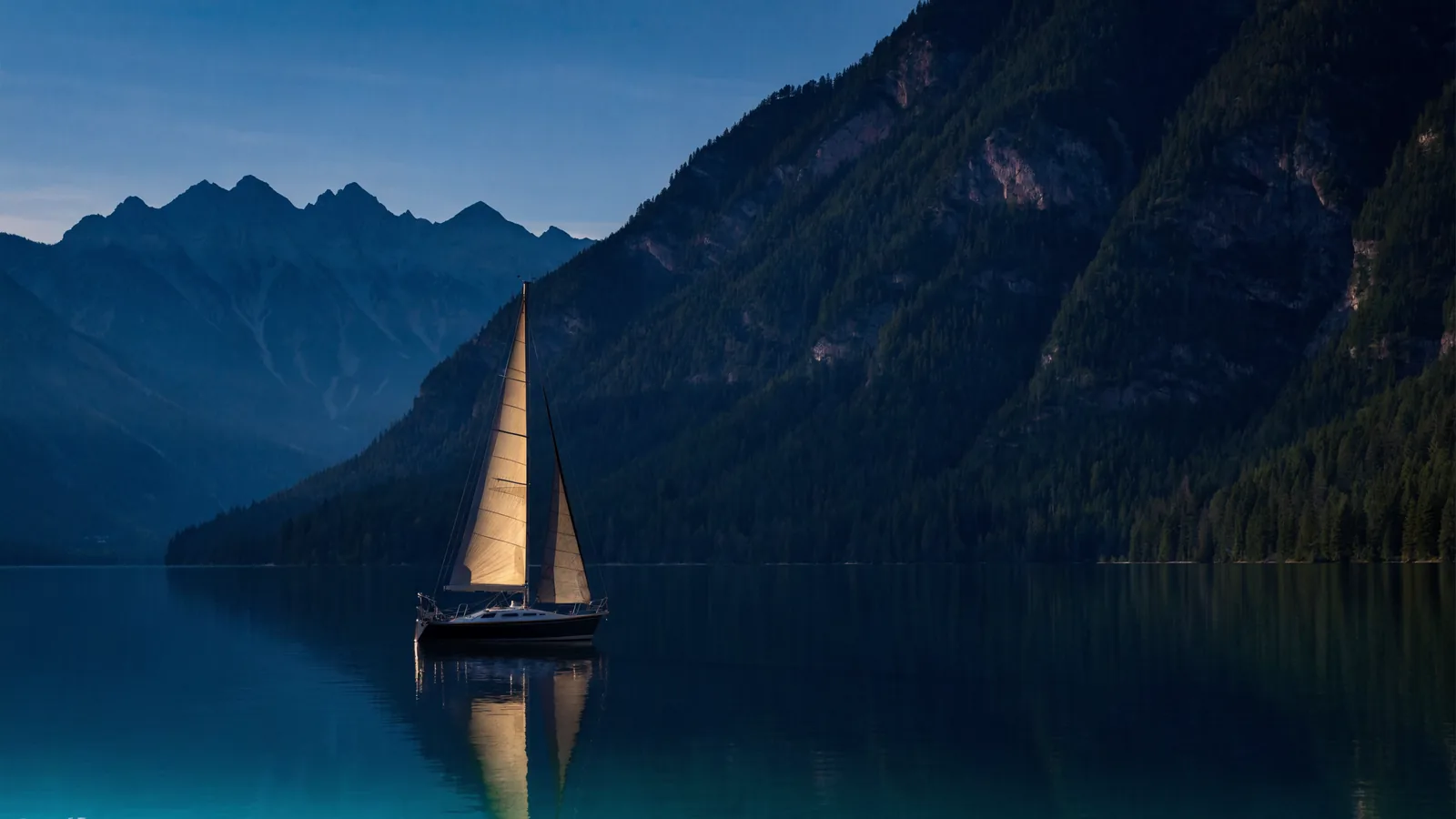 Segelboot auf einem Alpensee vor bewaldeten Bergen