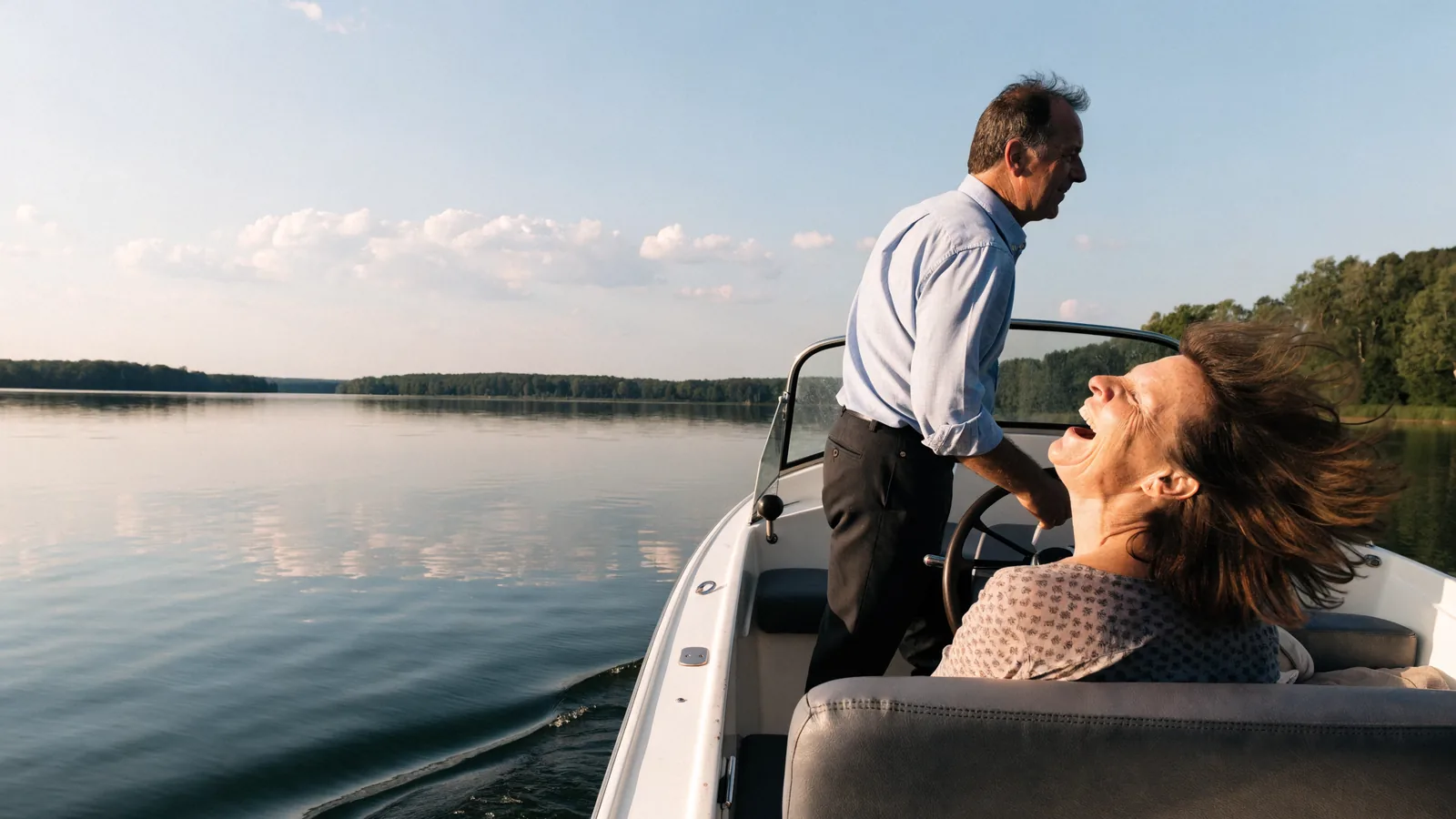 Ein Paar auf dem eigenen Motorboot: er steht am Steuer, sie lacht mit dem Wind im Haar, ein See im Sommerlicht