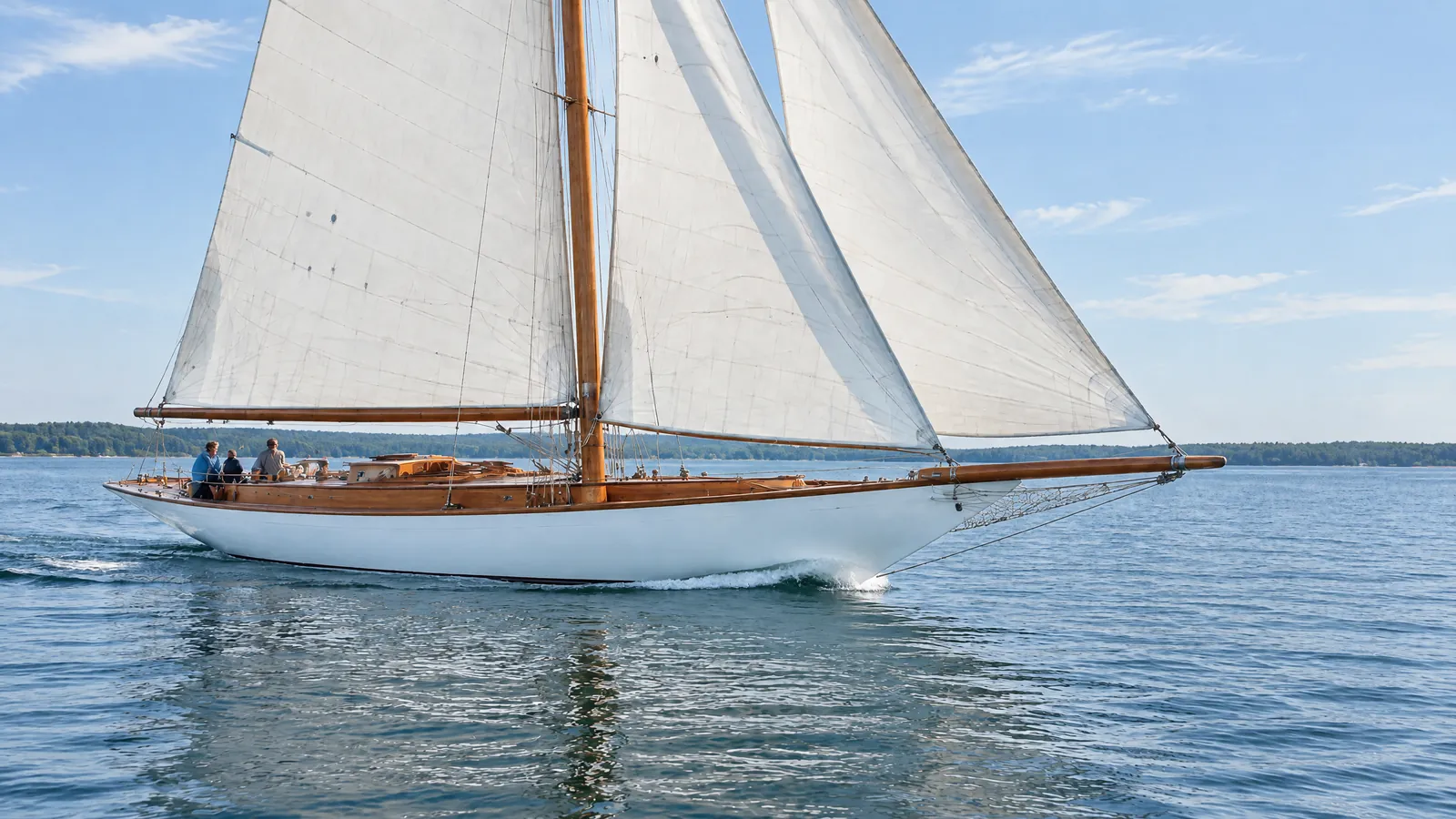 Klassische Holz-Segelyacht aus den 1930er Jahren mit lackiertem Mast unter Segeln im Abendlicht