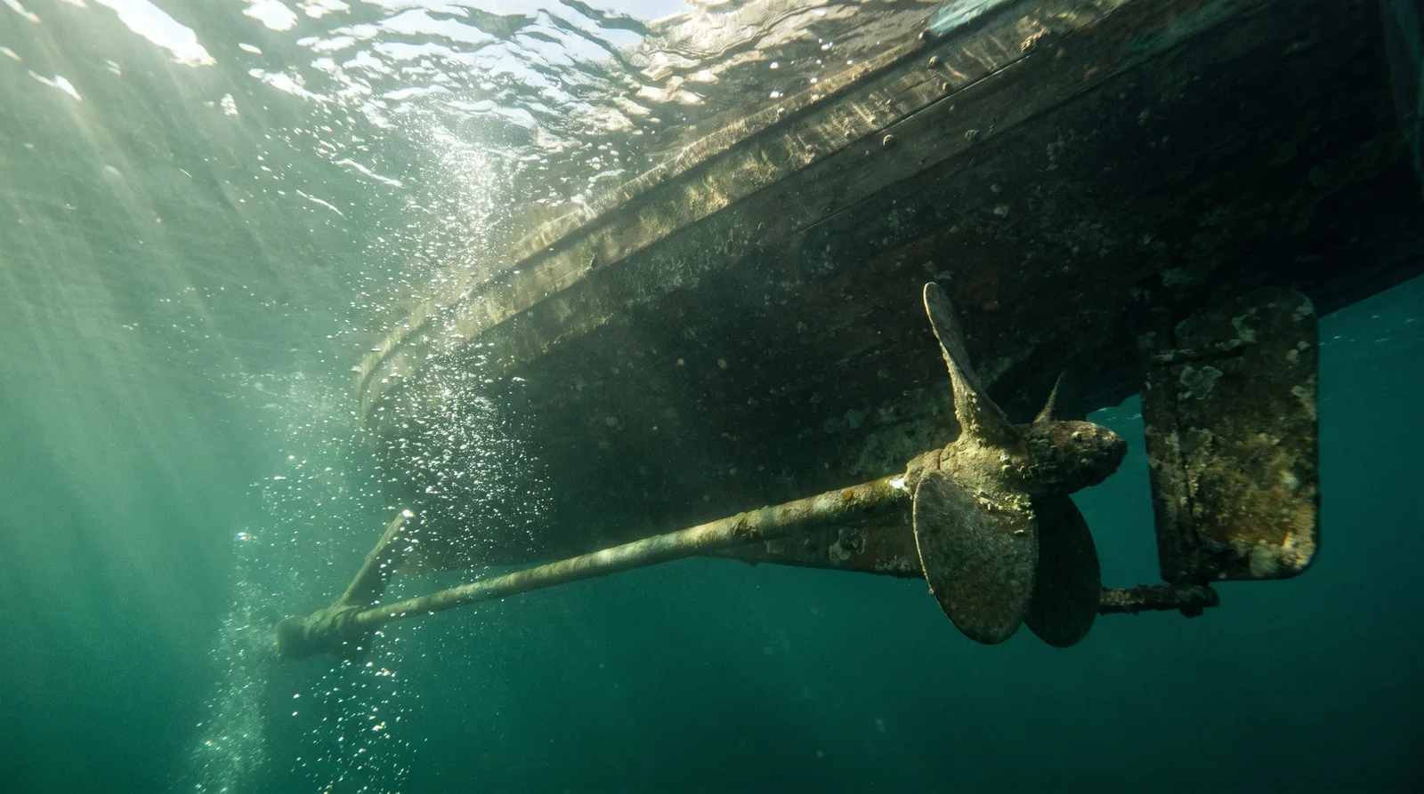 An underwater view of the propeller and hull of a boat under way