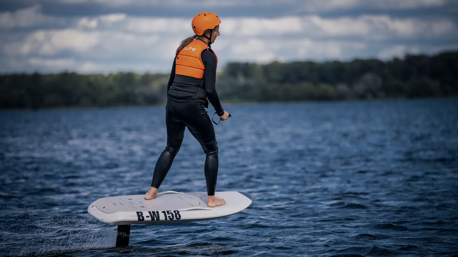 Fahrerin auf einem E-Foil, das Board schwebt über dem Wasser, der Flügelmast steht frei in der Strömung