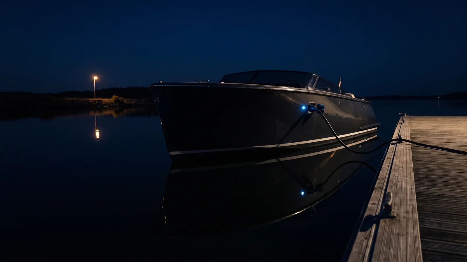 Elektroboot nachts am Steg, Ladekabel im Rumpf