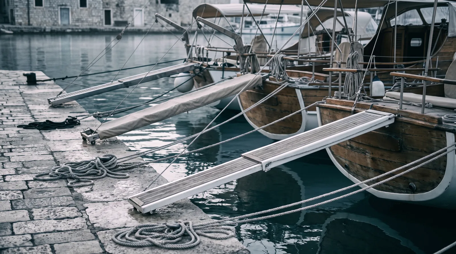 A row of yacht sterns moored to a stone quay, boarding gangways lowered onto the stone
