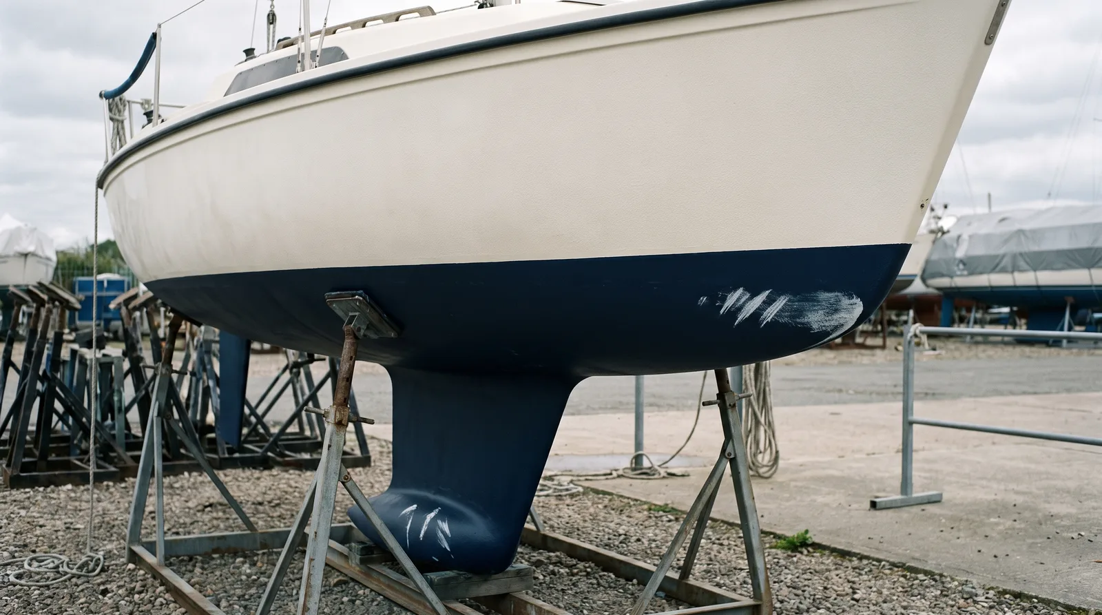 Kiel eines kleinen Segelboots auf einem Lagerbock in einer Werft, mit Schrammen an der Kielunterseite.