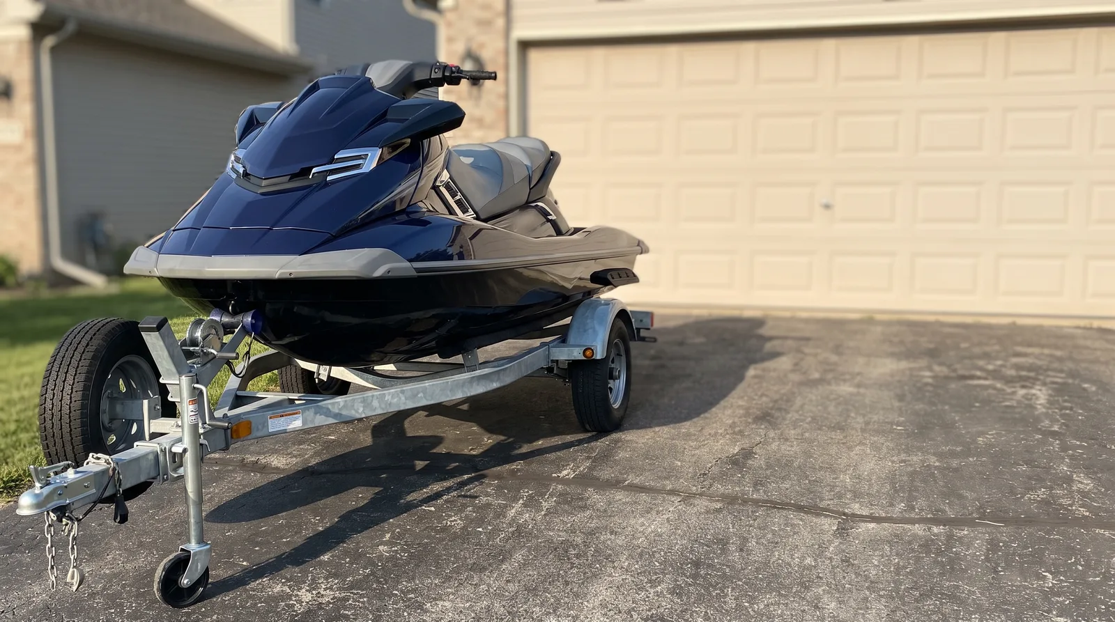 Ein moderner Jetski steht auf einem Trailer in einer gepflasterten Einfahrt vor einer Garage, weiches Morgenlicht.