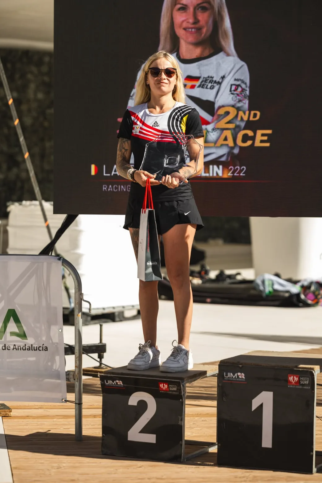 Laureen Thellin Deprez on the podium holding her trophy, the screen behind her showing second place
