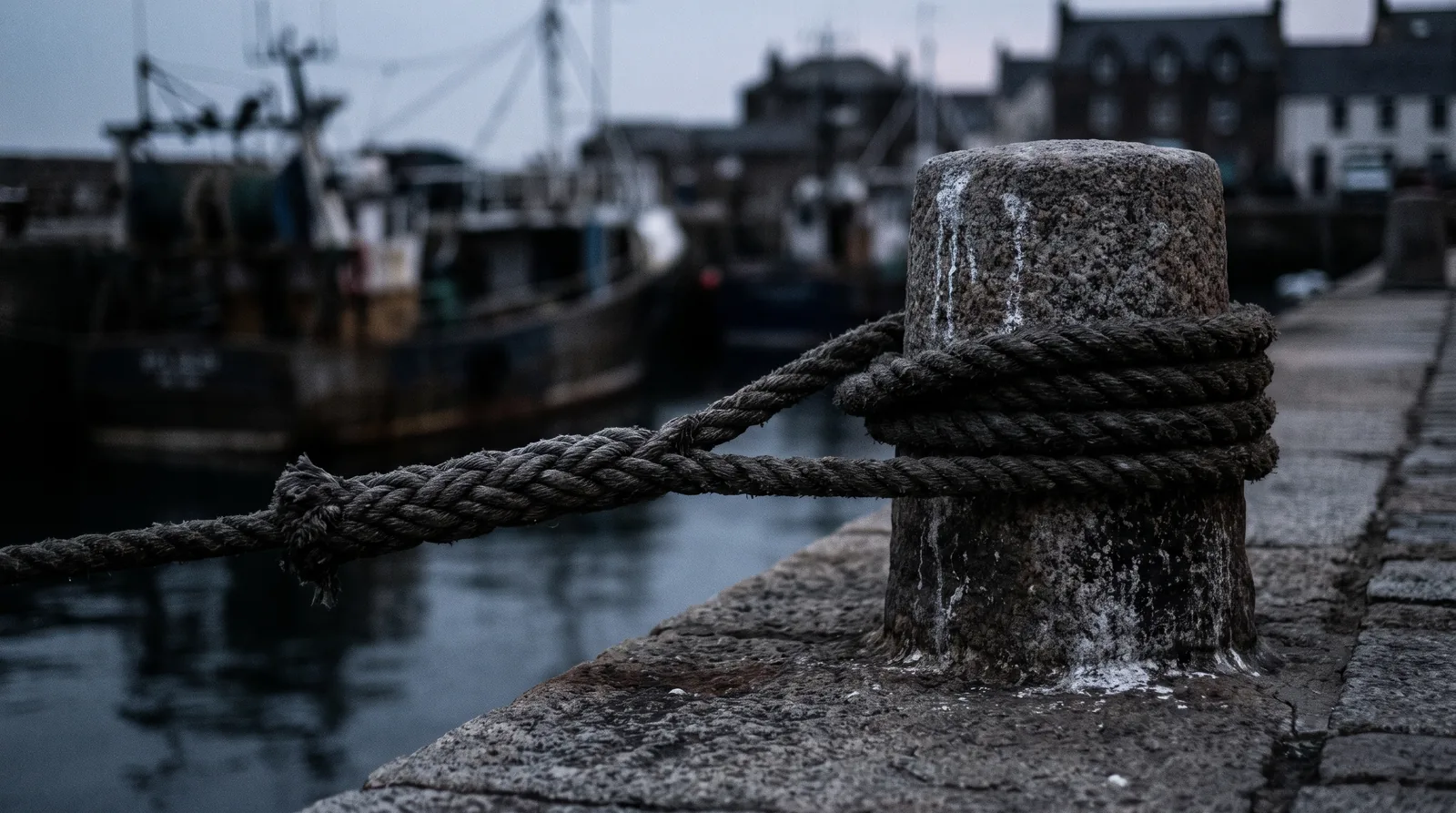 A heavy spliced mooring line turned around a granite bollard on a quay