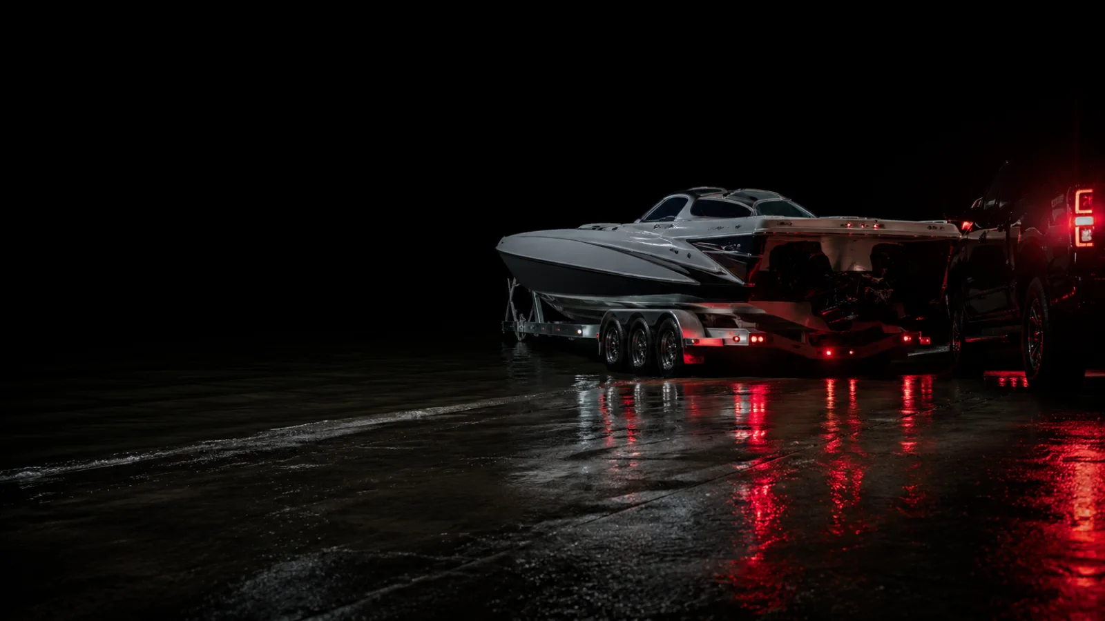 Motorboot auf dem Trailer an der nassen Rampe bei Nacht, Zugfahrzeug mit Rücklichtern