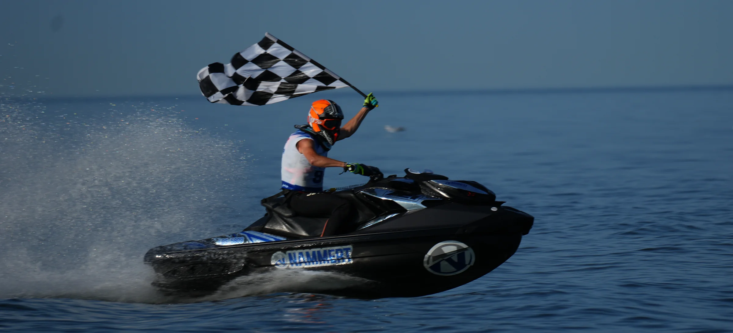 Jet ski rider with the NAMMERT logo and a start number waving the chequered flag at the finish
