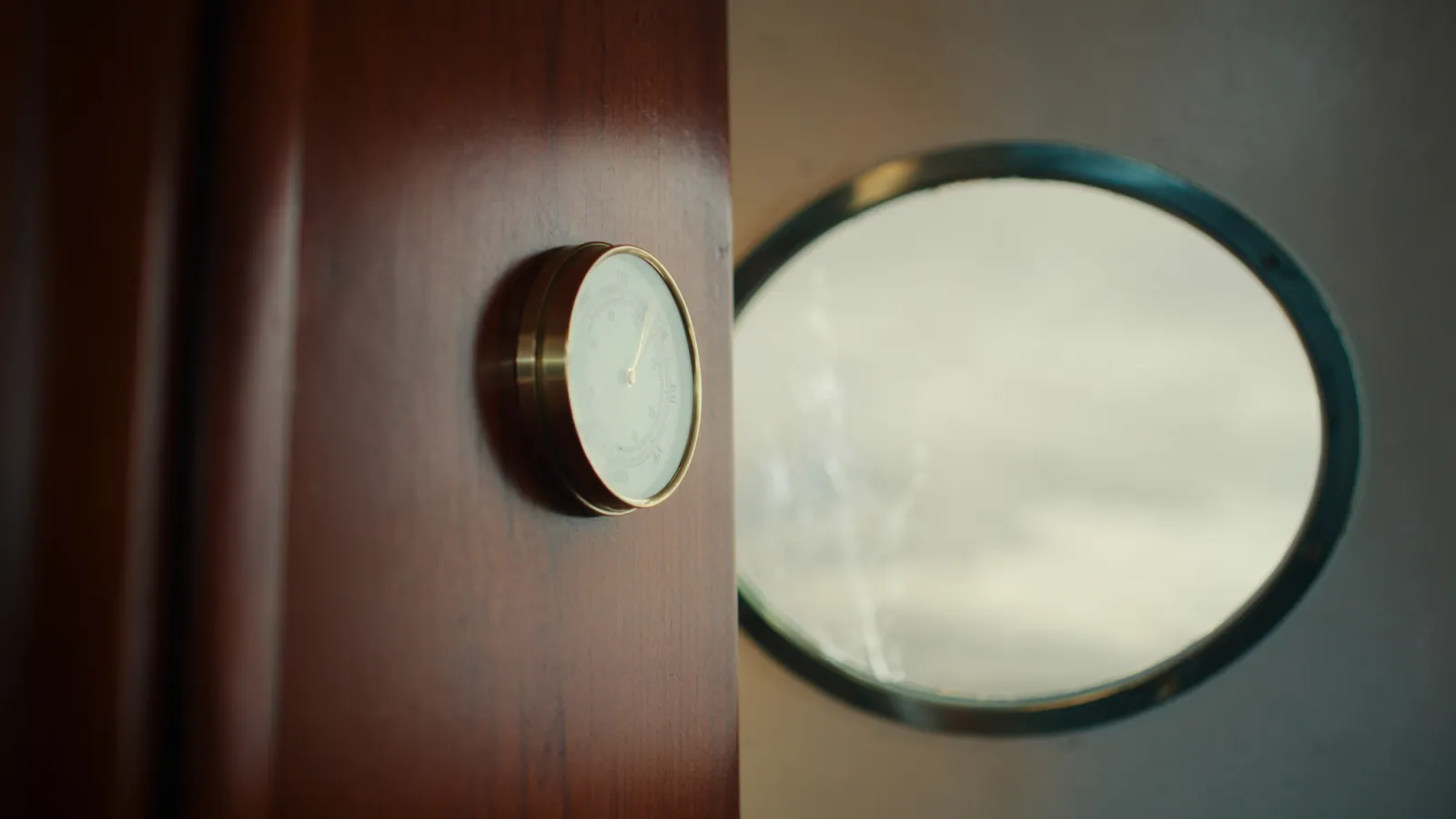 A ship's barometer on a bulkhead, grey sky through the porthole