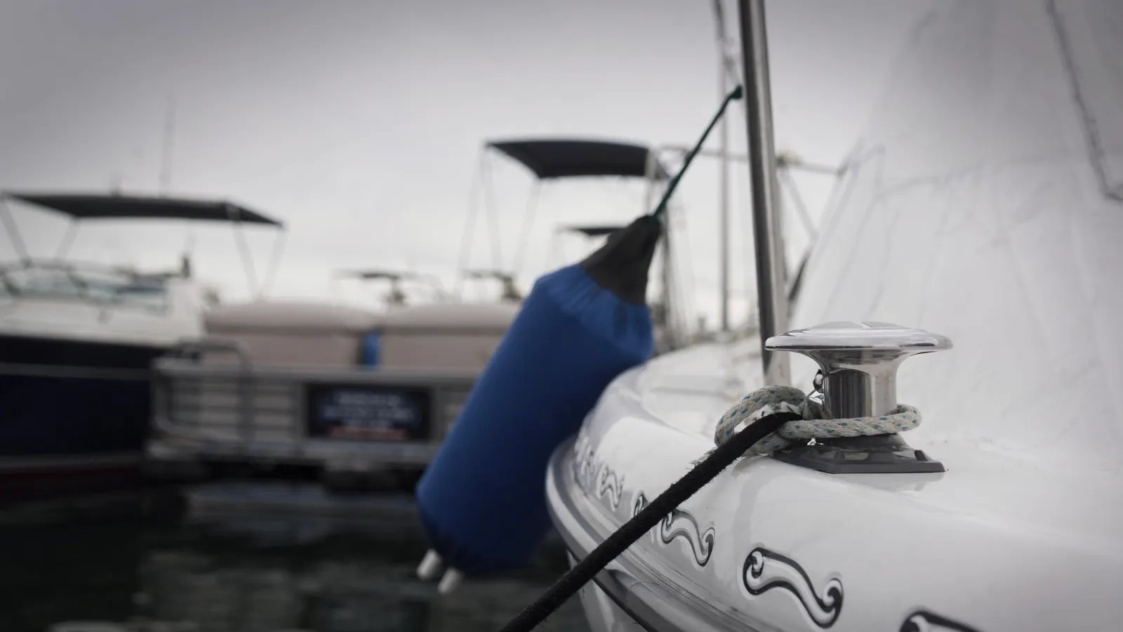 A mooring line on a cleat, a blue fender against the hull, marina behind
