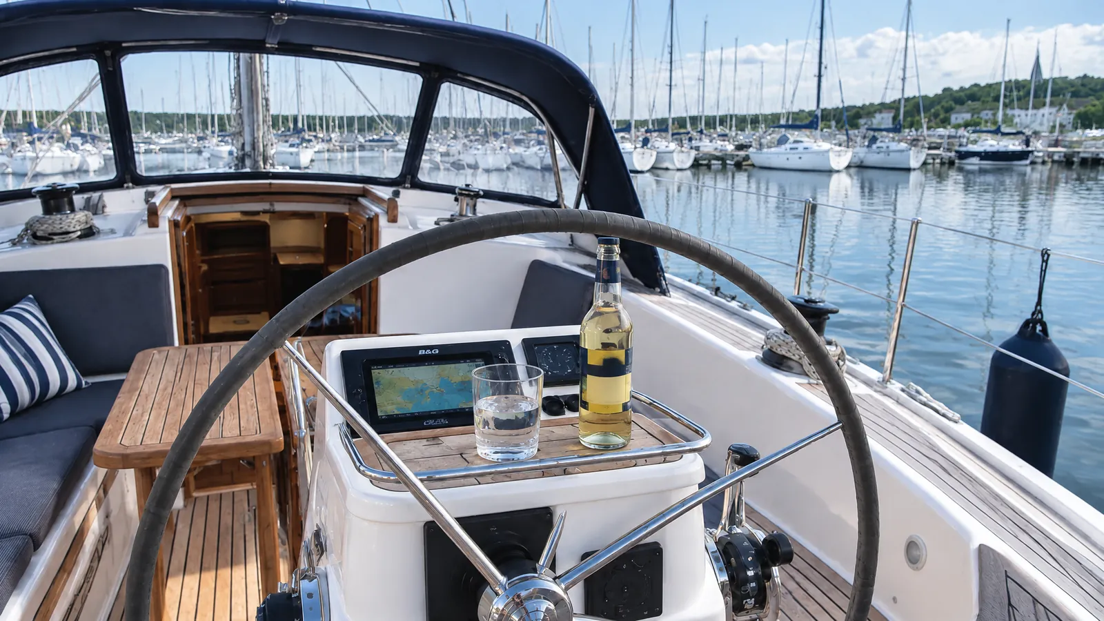 Cockpit einer Segelyacht in der Sonne, am Steuerstand stehen ein Glas Wasser und ein alkoholfreies Getränk