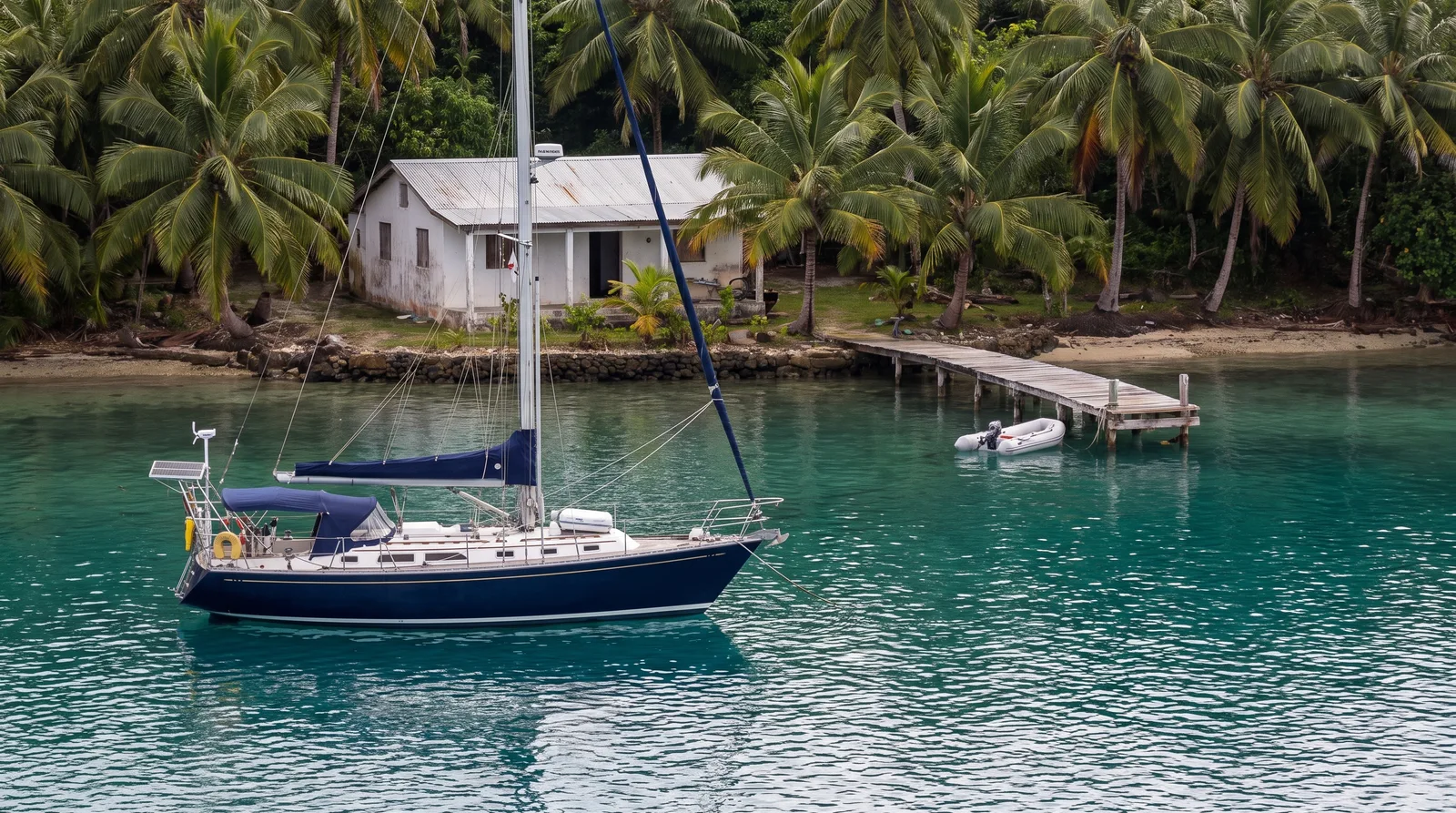 Fahrtenyacht vor Anker in einer tropischen Bucht mit kleiner Klinik am Ufer