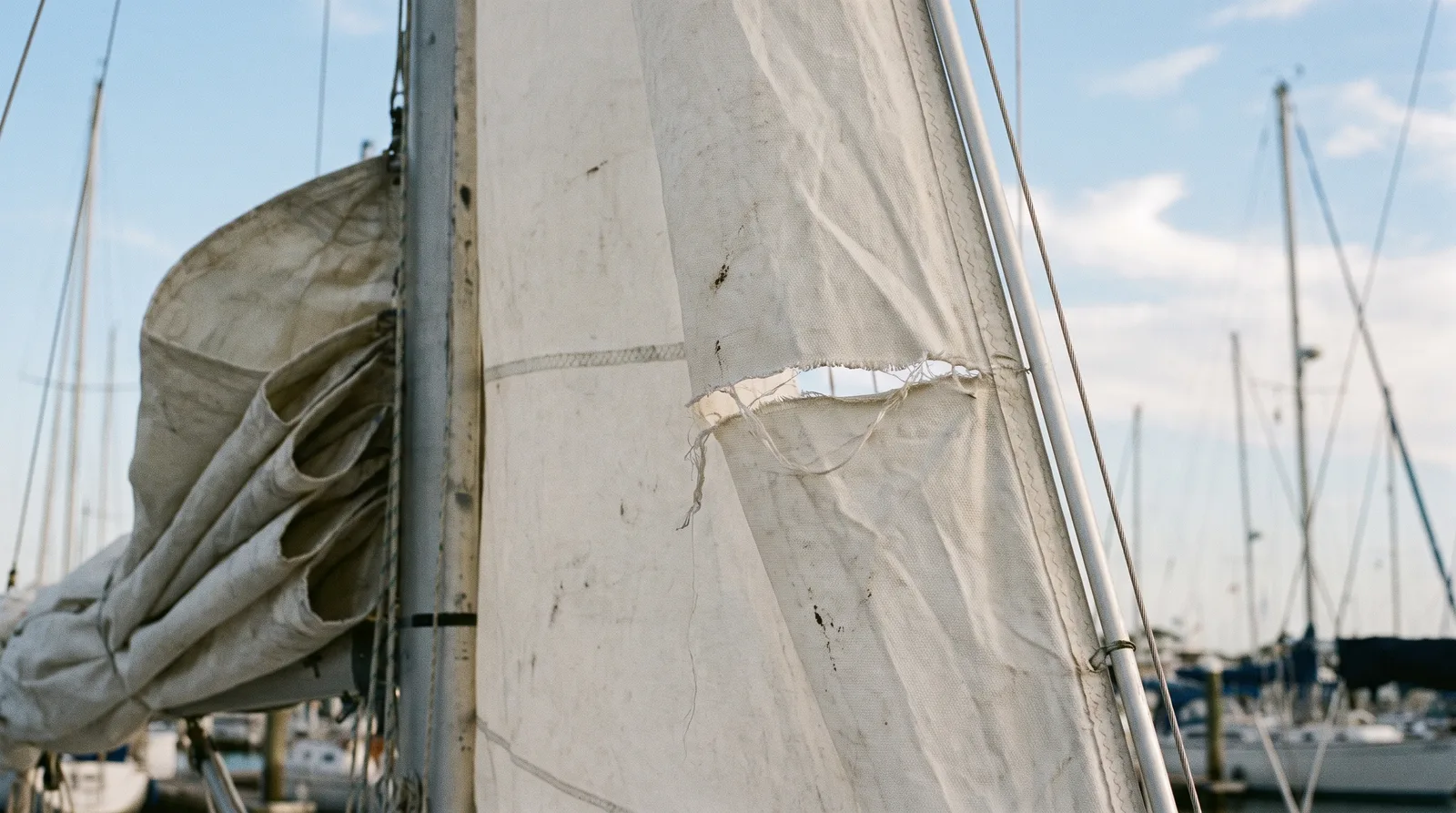 Weißes Vorsegel einer Charteryacht mit einem deutlichen Riss nahe dem Achterliek, teilweise eingerollt am Vorstag vor blauem Himmel