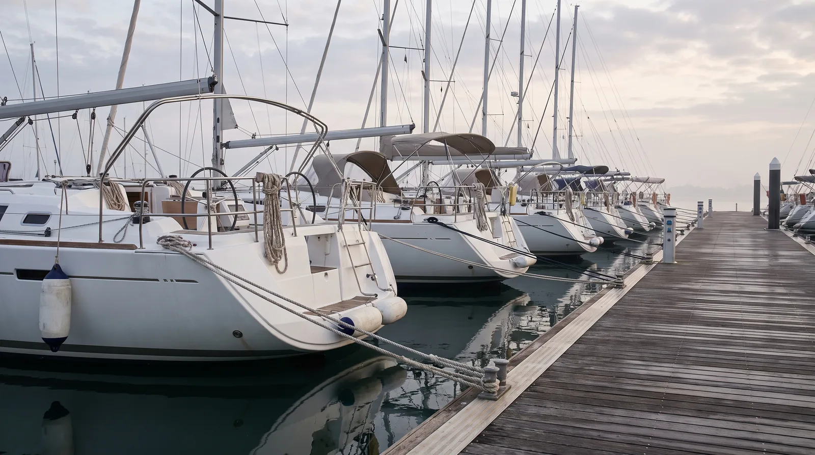 Reihe gleicher Charteryachten mit dem Heck am Steg einer Marina im Morgenlicht