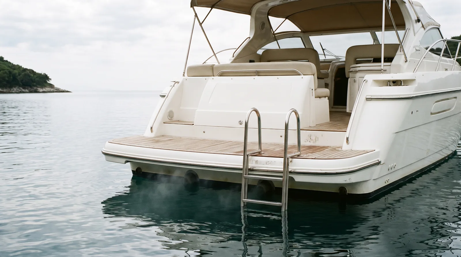 Heck einer gepflegten Motoryacht vor Anker mit Badeplattform, Badeleiter und Auspufföffnungen knapp über dem Wasser
