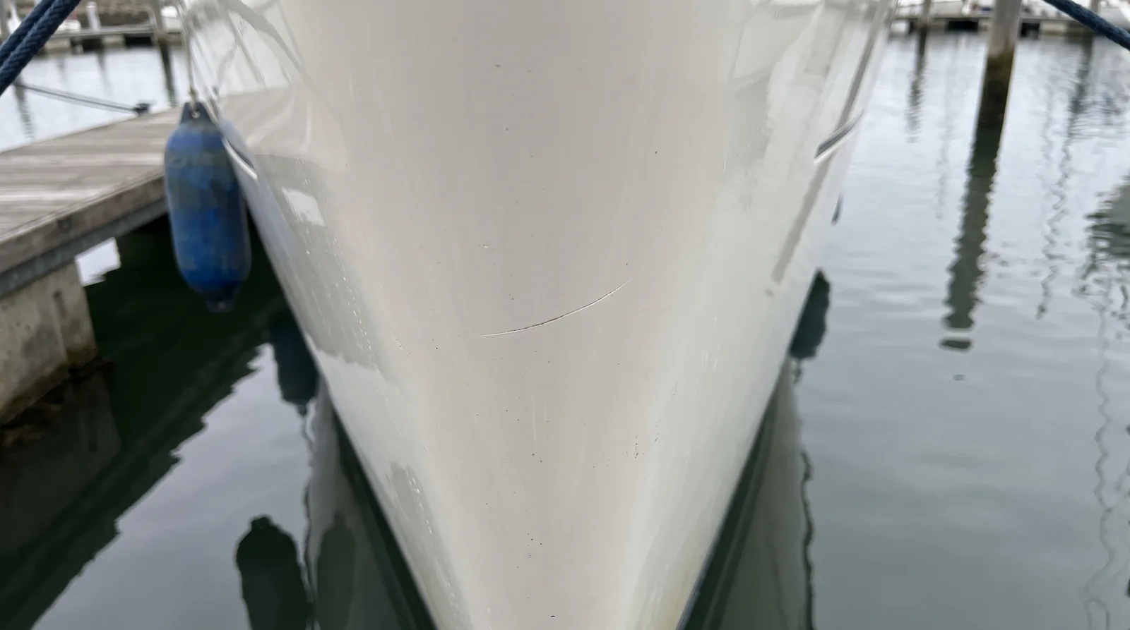 Fine scratch in the white gelcoat near the bow of a yacht, next to a fender