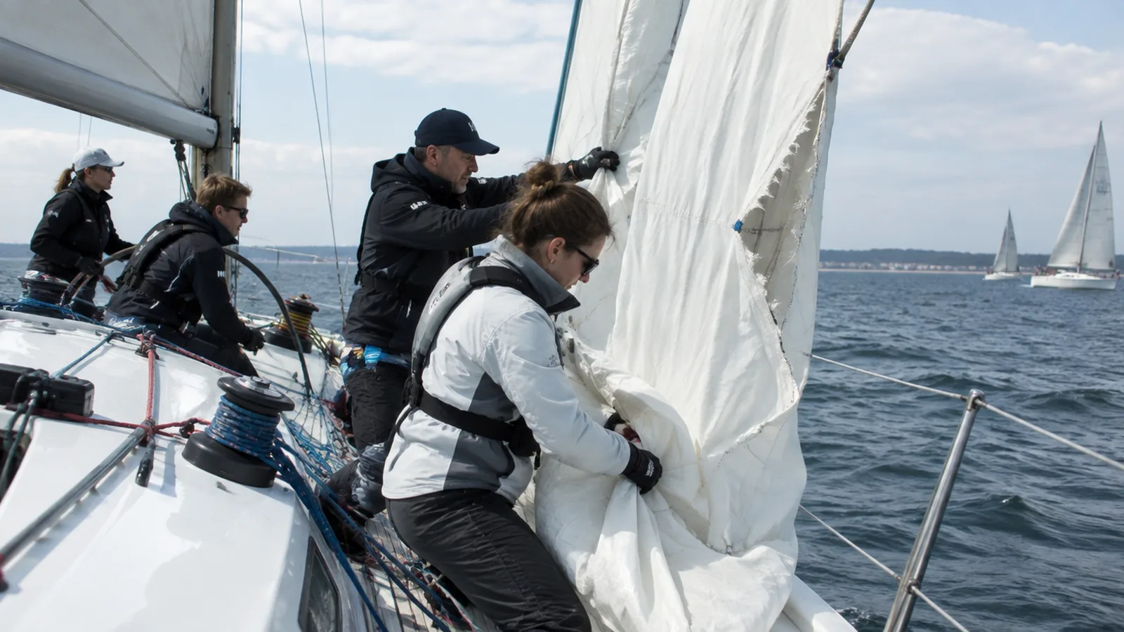 The crew of a racing yacht recovering a badly torn headsail on the foredeck