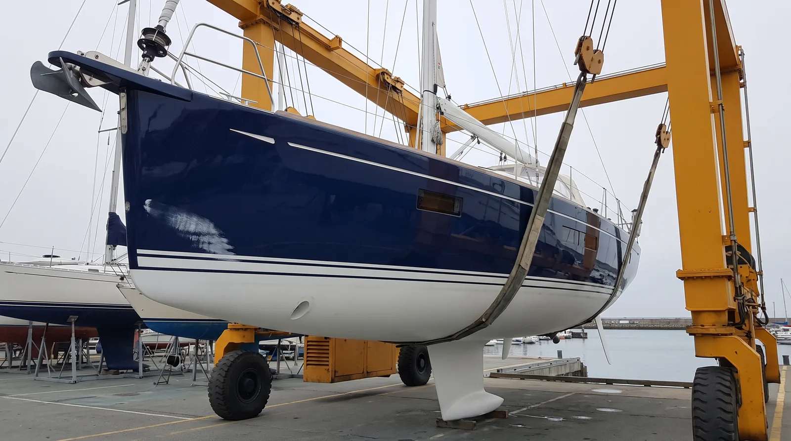 Well kept blue sailing yacht hanging in the travel lift of a yard, lifted out for repair