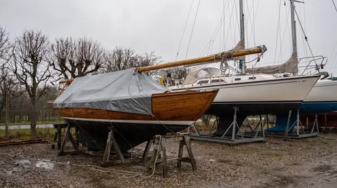 Winterlager an Land: eine Segelyacht mit stehendem Mast auf dem Lagerbock, daneben ein Boot mit gelegtem Mast auf Holzböcken
