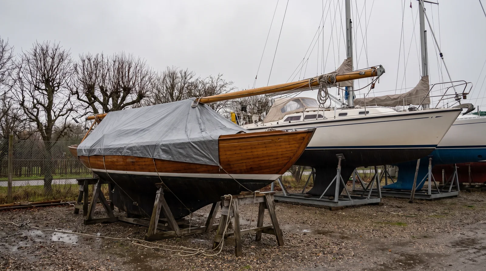 Winterlager an Land: eine Segelyacht mit stehendem Mast auf dem Lagerbock, daneben ein Boot mit gelegtem Mast auf Holzböcken