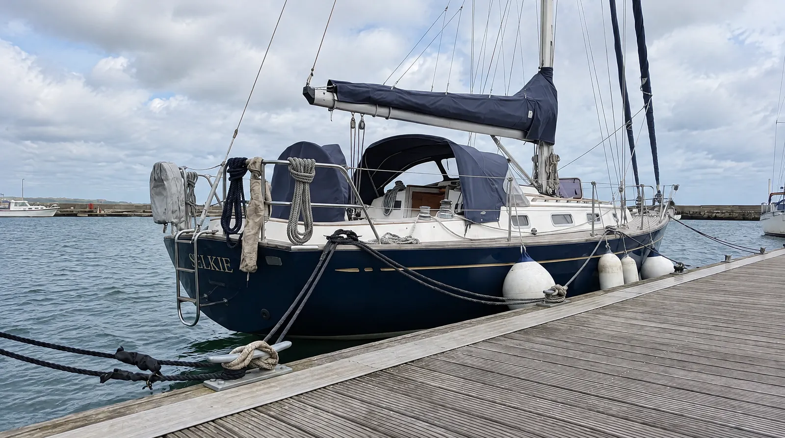 A sailing yacht at the dock, doubled lines, fenders out, sails stowed, weather building behind