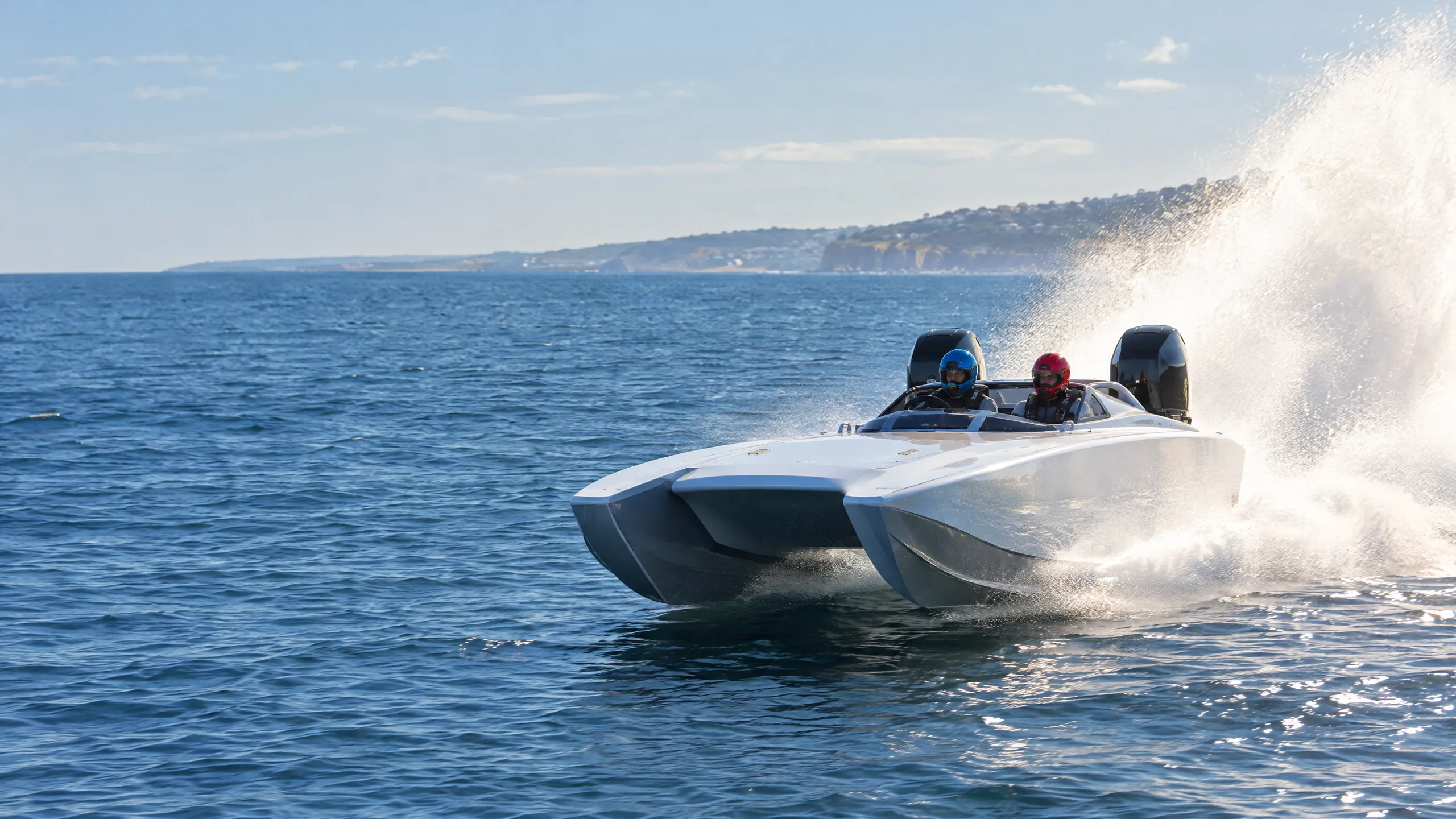 A white racing catamaran with twin outboards flies across the sea, two helmeted drivers aboard, spray flying behind