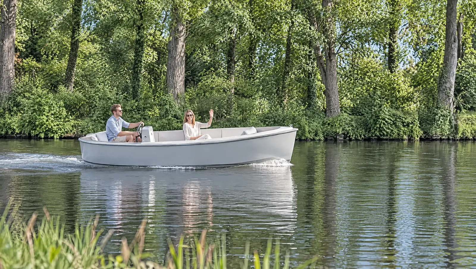 Light grey electric boat glides along a tree-lined canal in sunshine, he steers, she laughs and waves to the bank